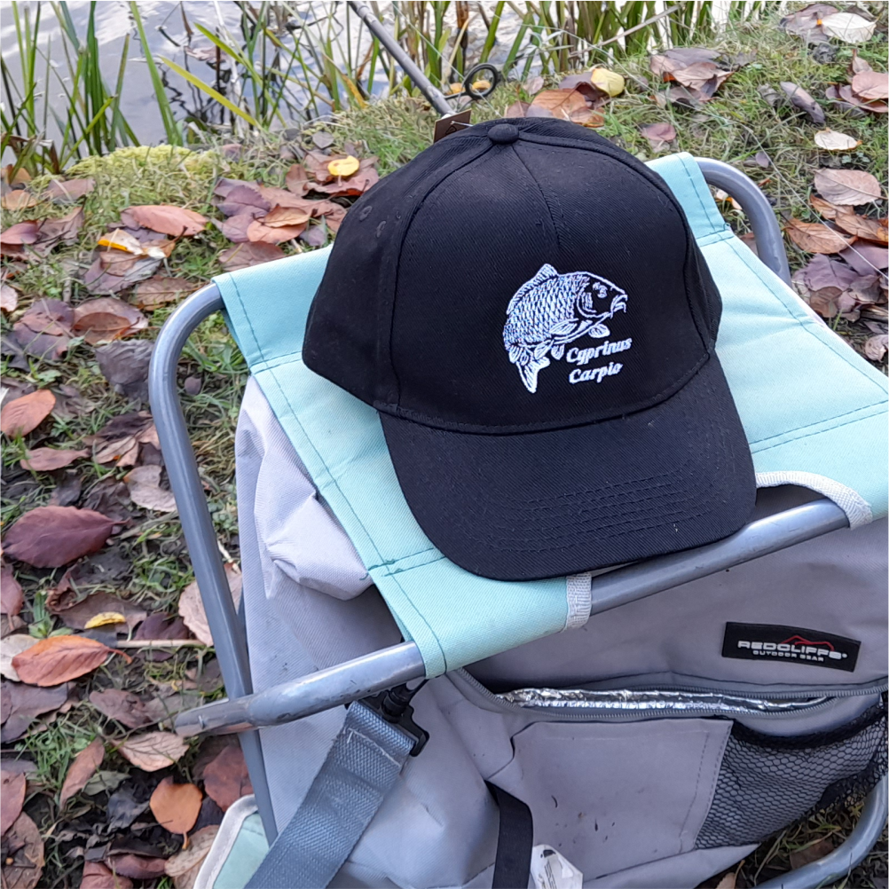 Black carp fishing cap placed on outdoor chair – embroidered carp logo angler hat