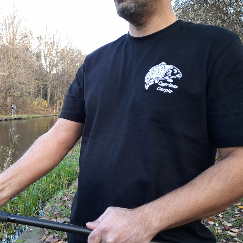 Black fishing t-shirt with embroidered carp logo worn outdoors while holding a fishing rod